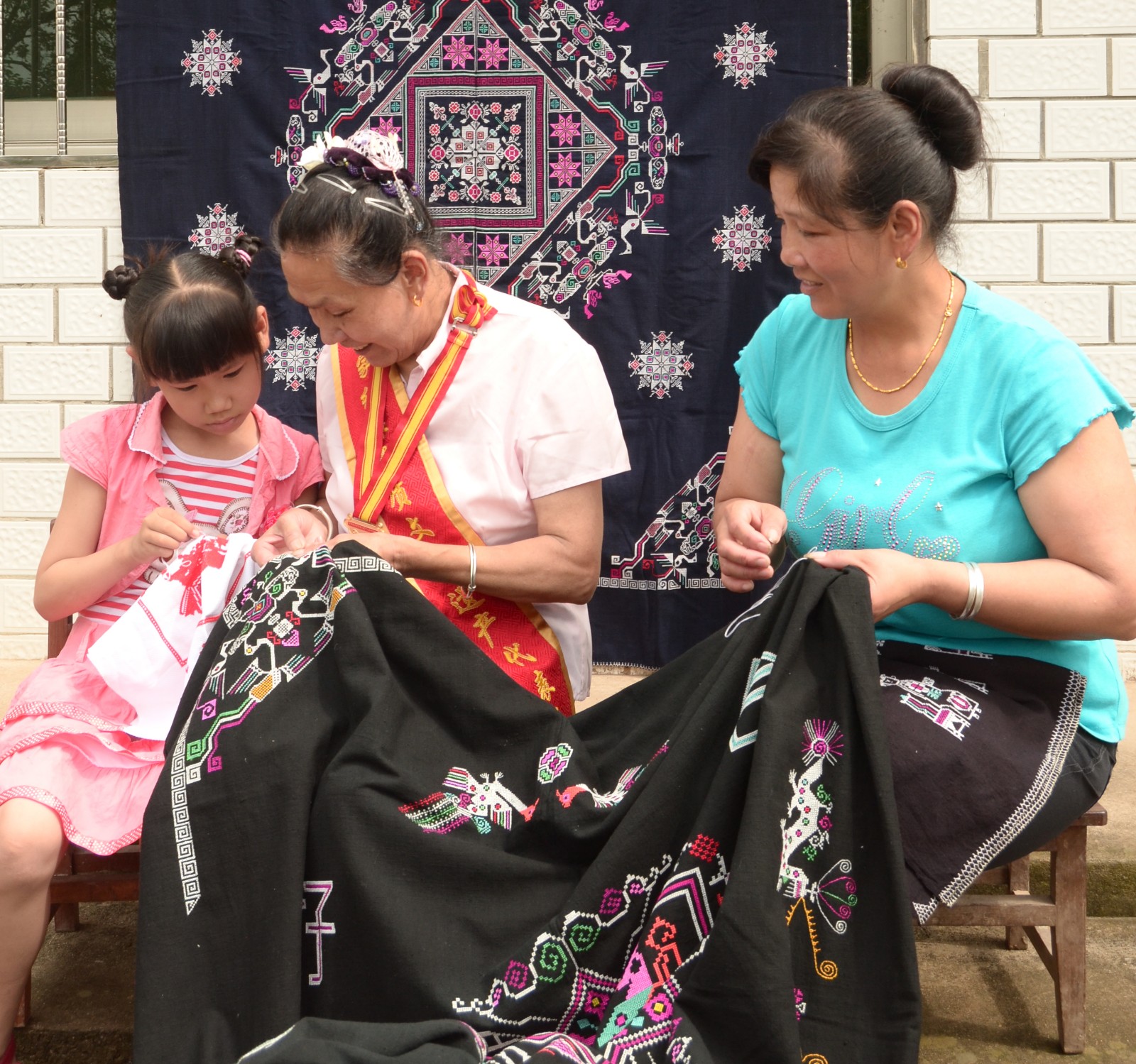 图为石九梅向女儿陈韶君及外甥女传授挑花技艺.梅新南摄